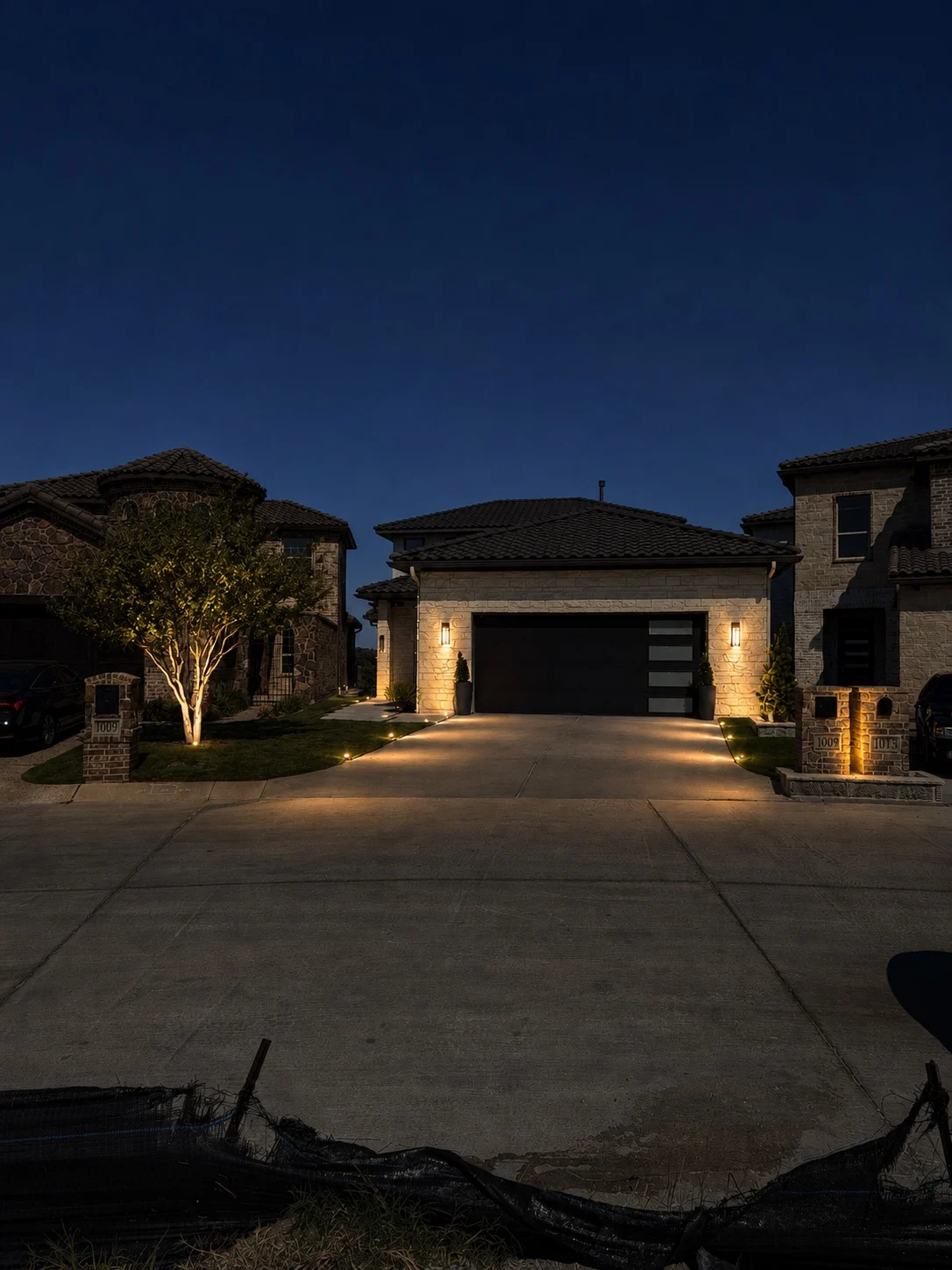 Shielded driveway light, tree accents, and a warm architectural wash.